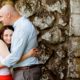 Duke Farms engagement photograph: couple hugs with moss-covered stone wall in background; woman wears lipstick-red skirt