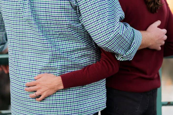 Close-up of couple hugging each other (no faces); man wearing blue checked shirt, woman wearing burgundy sweater. Engagement photo detail shot in Brooklyn, NY.