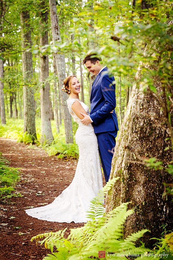 Bride and groom smile on mulched path in wooded area at Woodloch Pines resort, Castle Couture bridal gown, dark blue groom's suit, outdoor wedding photographer.