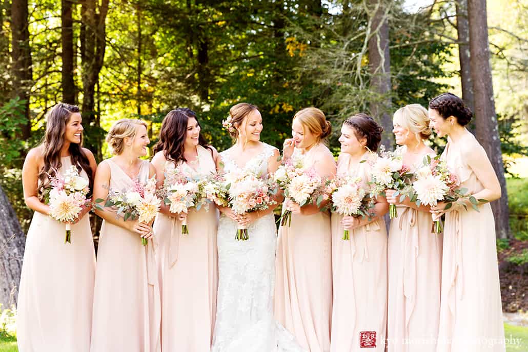 Bride and six bridesmaids gather in wooded area at Woodloch Pines in the Poconos, sand colored chiffon bridesmaids dresses by Nouvelle Amsale, Castle Couture bridal gown, pale pink dahlia, eucalyptus bouquets by Fox Hill Farm Experience, outdoor wedding photographer.