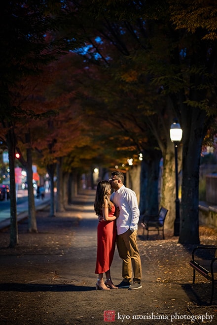 Princeton Nassau St NJ candid documentary engagement portrait session fall autumn a couple red dress European brick building wooded door street lights hold each other hug kiss on her fore head