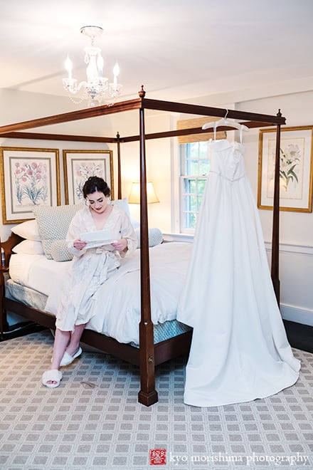 at Fall The Inn at Fernbrook Farm Chesterfield NJ Wedding bride reads a letter from groom on a bed with dress hanging in a bridal suite room