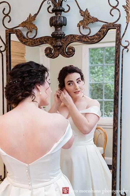 at Fall The Inn at Fernbrook Farm Chesterfield NJ Wedding bride in her dress putting her earring looking at herself reflection big mirror while getting ready in a bridal suite room