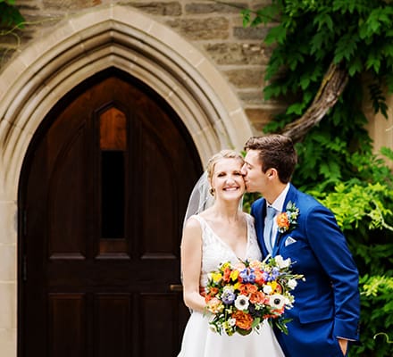 spring Princeton University campus wedding groom kisses her newly wife bride on her cheek smiling beautiful architecture with vine