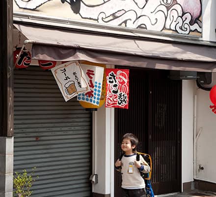A boy smiling walking by a Takoyaki restaurant, Japan