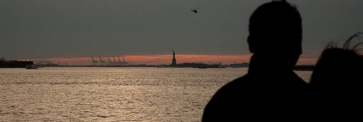 Sunset over New York Harbor with Statue of Liberty silhouette.